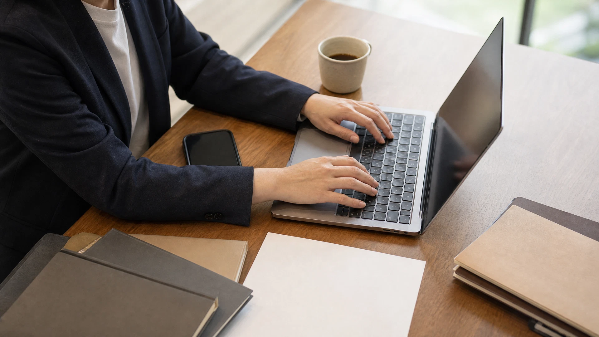 経営者が複数の顧問先資料とノートPCを使って業務を整理している俯瞰写真
